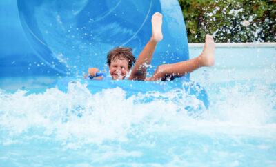 an 8 year old boy is riding in the water Park on inflatable circles on water slides; Farm Bureau Members Save